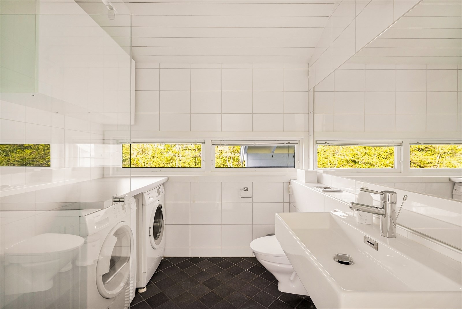 Badet er innredet med vegghengt toalett, servant, dusj og har opplegg for vaskemaskin og tørketrommel. Galleribilde