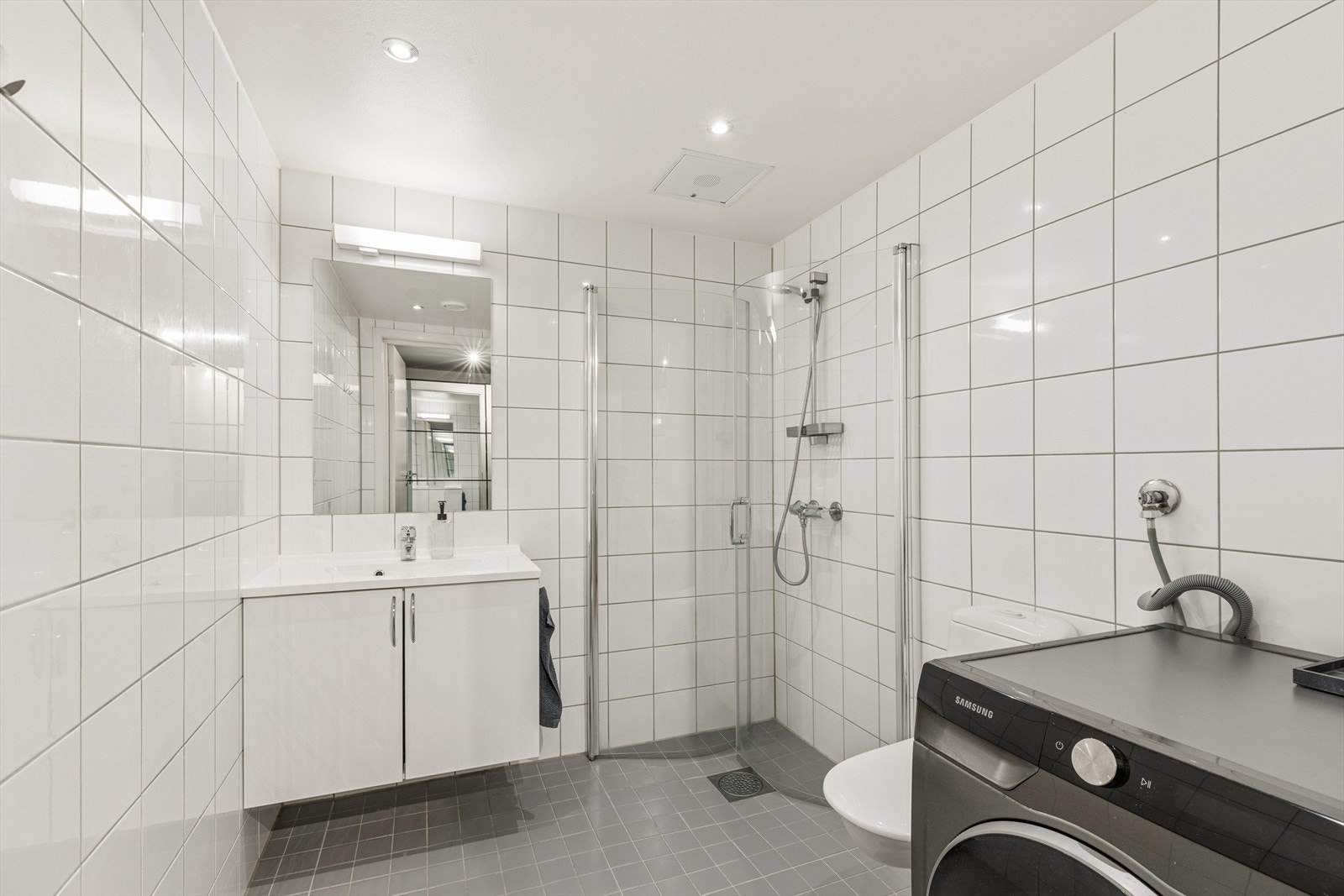 Badet er flislagt og utstyrt med dusj, servant, toalett og opplegg for vaskemaskin Galleribilde