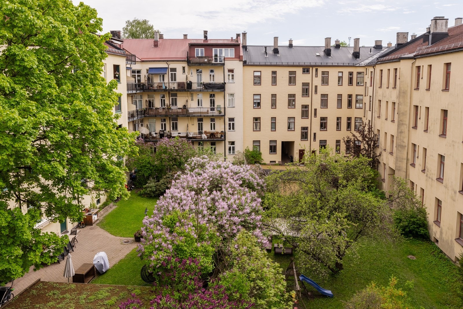 Herfra nyter man et nydelig utsyn mot bakgård og parkmessige grøntområder med syrintrær og frodig beplantning som skaper en lun og skjermet atmosfære. Galleribilde
