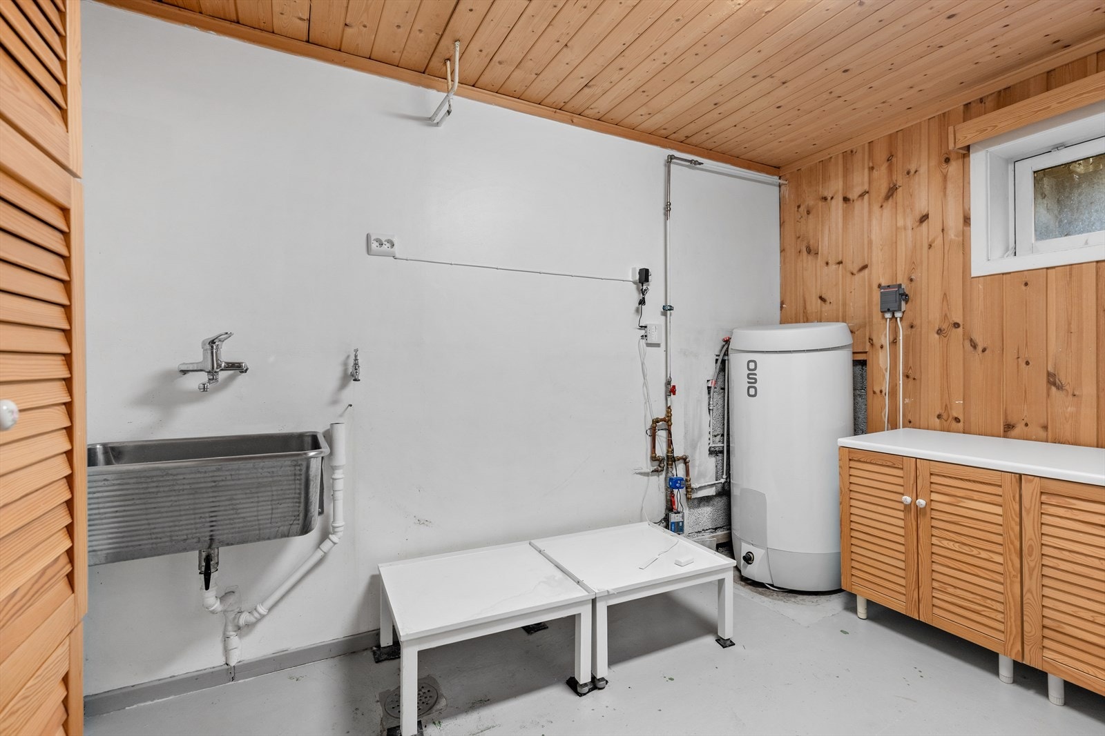 Praktisk vaskekjeller med utslagsvask, sluk i gulvet og en nyere varmtvannsbereder fra 2023. Galleribilde