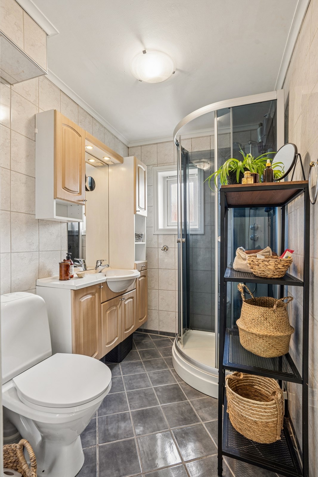 Badet er flislagt på veggene og utstyrt med nedfelt servant med tilhørende vegghengt speil og belysning, samt et gulvmontert toalett og dusjkabinett. Galleribilde