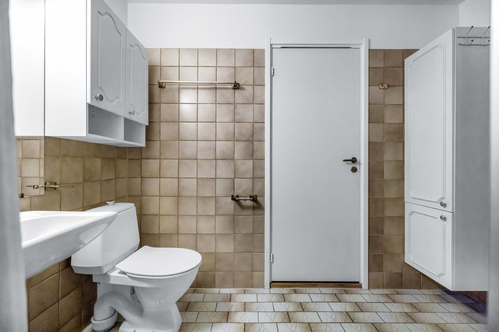 Badet er innredet med dusj, gulvstående toalett, vegghengt servant med armatur, opplegg for vaskemaskin, speil og baderomsinnredning med hvite profilerte fronter. Galleribilde