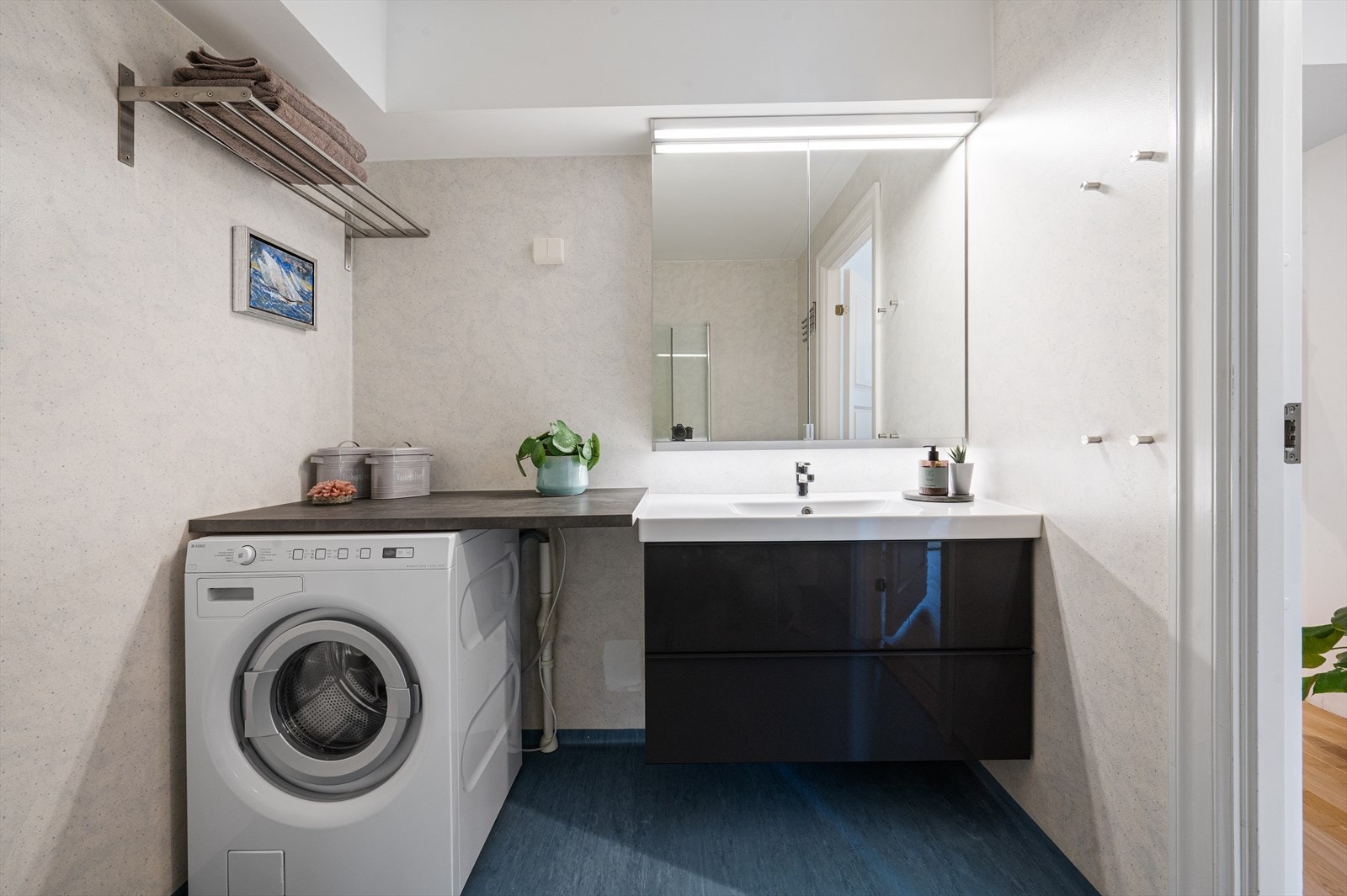 Pen servant med underliggende skuffer og vegghengt speil med belysning. Badet har også opplegg for vaskemaskin og tørketrommel. Galleribilde