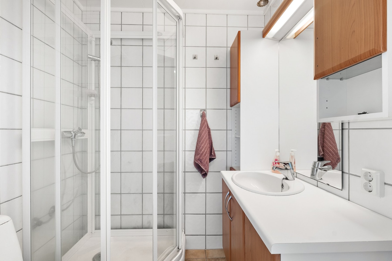 Badet i utleiedelen har fliser på gulv med gulvvarme, dusjkabinett og servant i innredning. Galleribilde