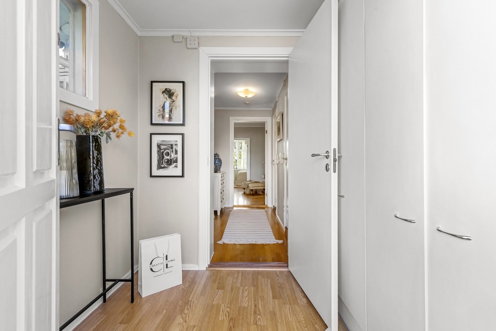 Fin entré med lysmalte vegger og gyllent laminatgulv. Yttertøyet ryddes enkelt bort i en bred garderobeløsning med hvite, glatte fronter. Galleribilde