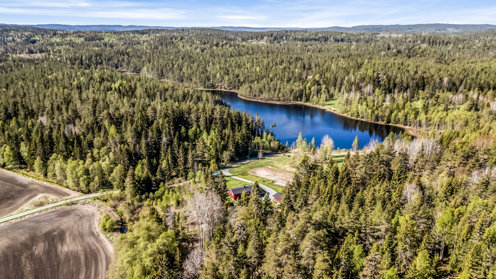 Boligen ligger i et skogsområde nær en innsjø, omgitt av frodige trær og åser. Galleribilde