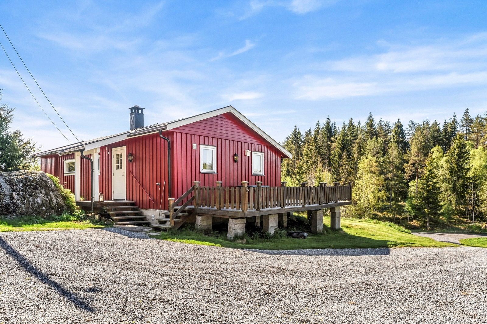 Fritidsbolig med terrasse, omgitt av natur og skog. Gruset gårdsplass foran huset. Galleribilde