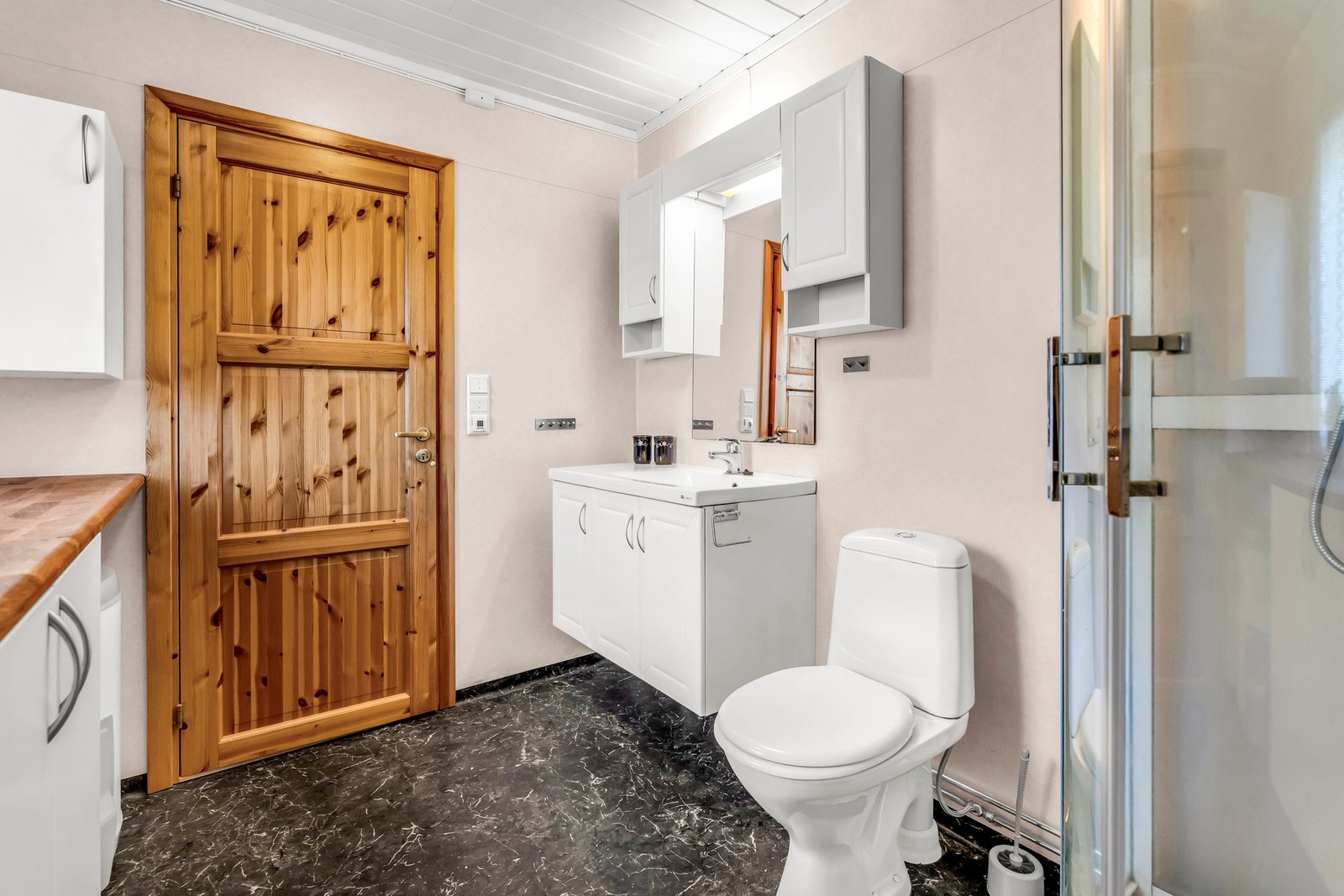 Badet har moderne innredning med dusjkabinett, toalett og servant med speilskap. Mørke fliser på gulvet. Galleribilde