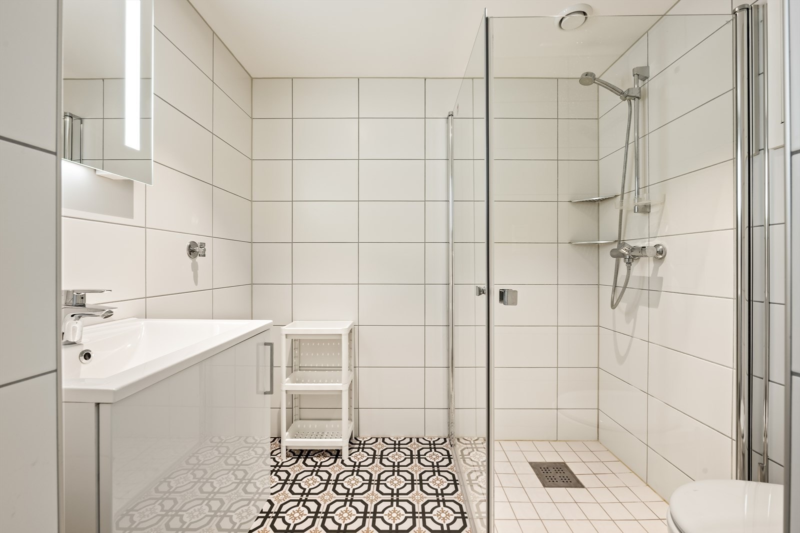 Badet er praktisk innredet med veggmontert toalett, dusjvegger/dusjhjørne og opplegg for vaskemaskin. Galleribilde