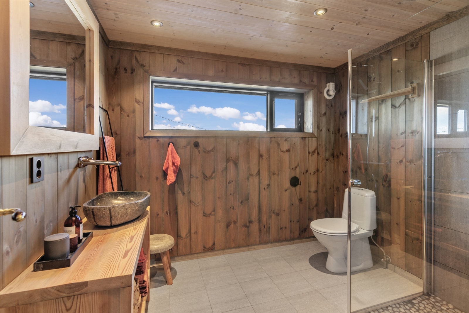 Badet har flislagt gulv med gulvvarme, innredning i tre og en toppmontert servant. Galleribilde