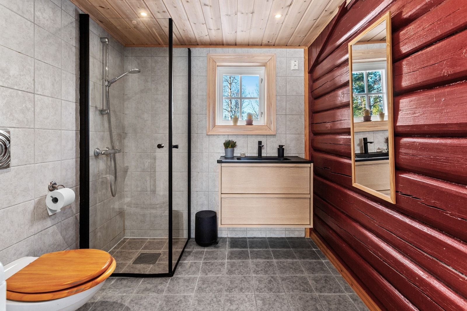 Badet har flis på gulv og flis og malt tømmer på vegger. Innvendig tak har panel. Rommet er utstyrt med innfellbare dusjdører, servantskap og opplegg for vaskemaskin. Galleribilde