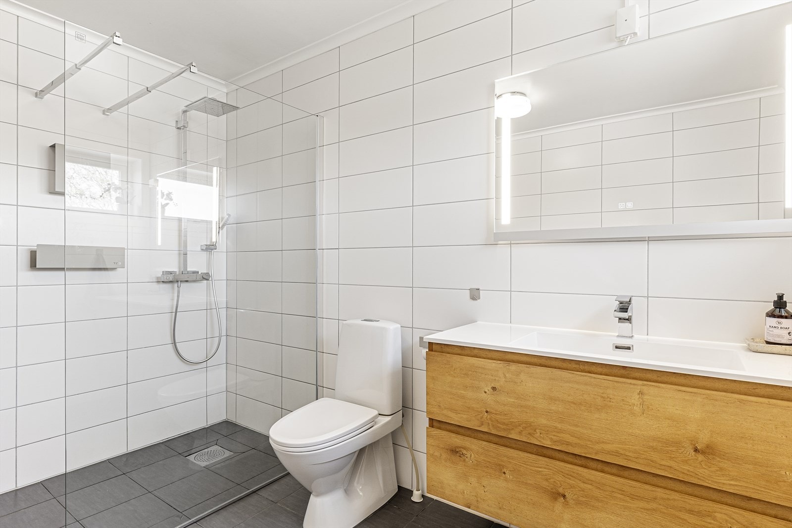 Badet er innredet med dusj på vegg med glassvegger, toalett og baderomsinnredning med nedfelt servant. Galleribilde