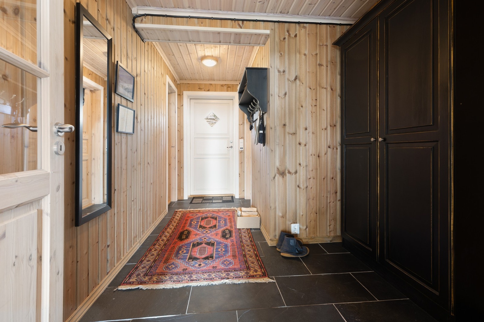 Romslig entré med flislagt gulv med varmekabler og vegger i trepanel som gir et lunt og innbydende uttrykk. Entréen har god plass til oppbevaring i garderobeskap og fungerer som en praktisk adkomstsone til hytta. Galleribilde