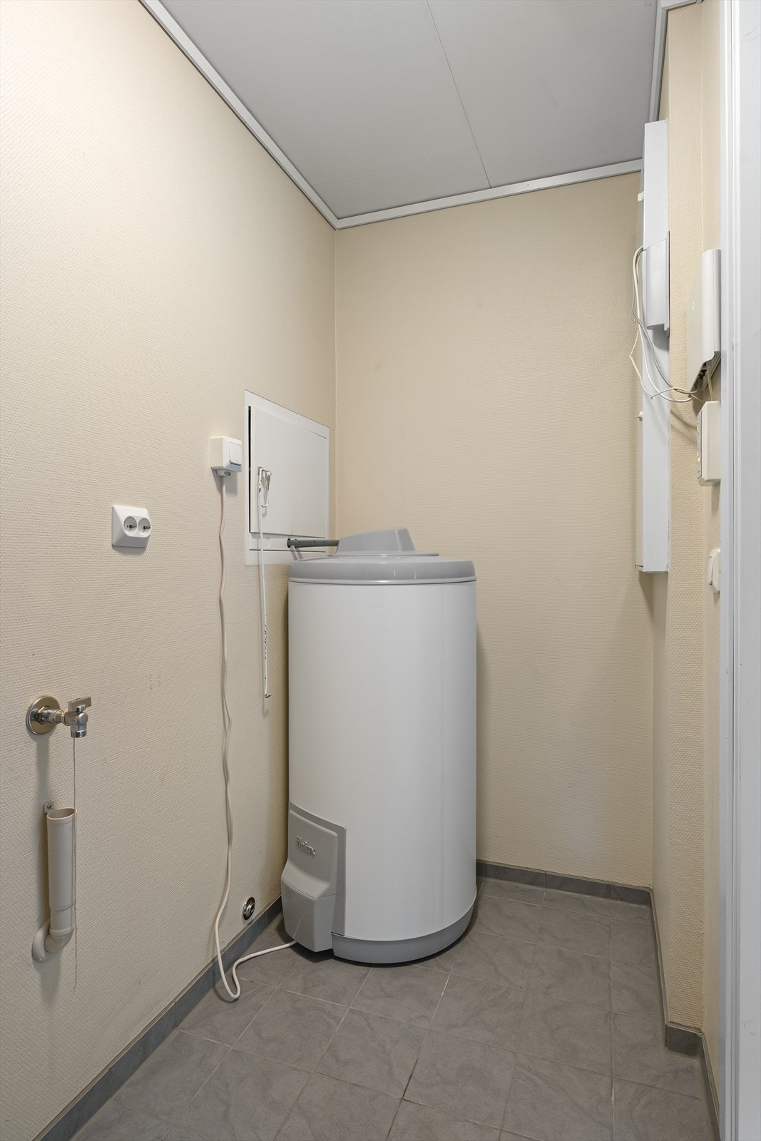 Praktisk vaskerom/bod med flislagt gulv, opplegg for vaskemaskin, varmtvannsbereder og sentralstøvsuger. Galleribilde