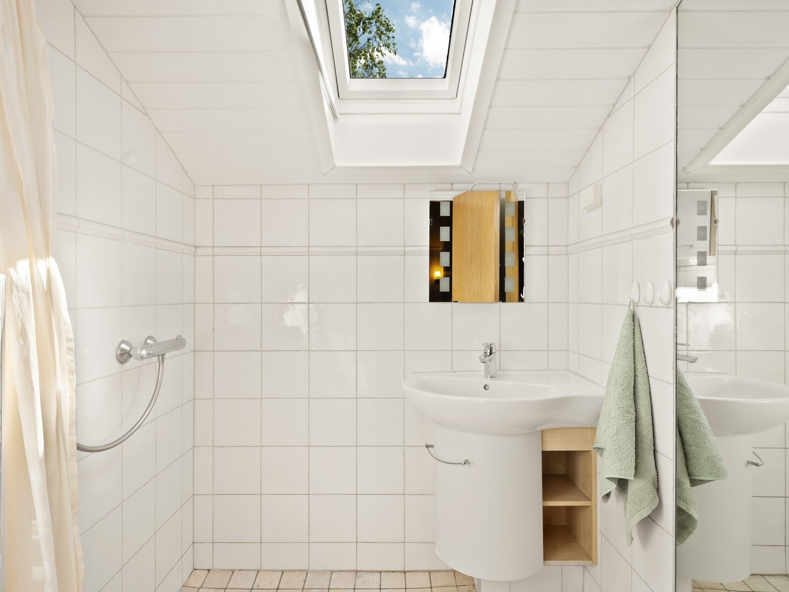 Badet har flislagte overflater, veggmontert toalett, servant og dusj med forheng. Galleribilde
