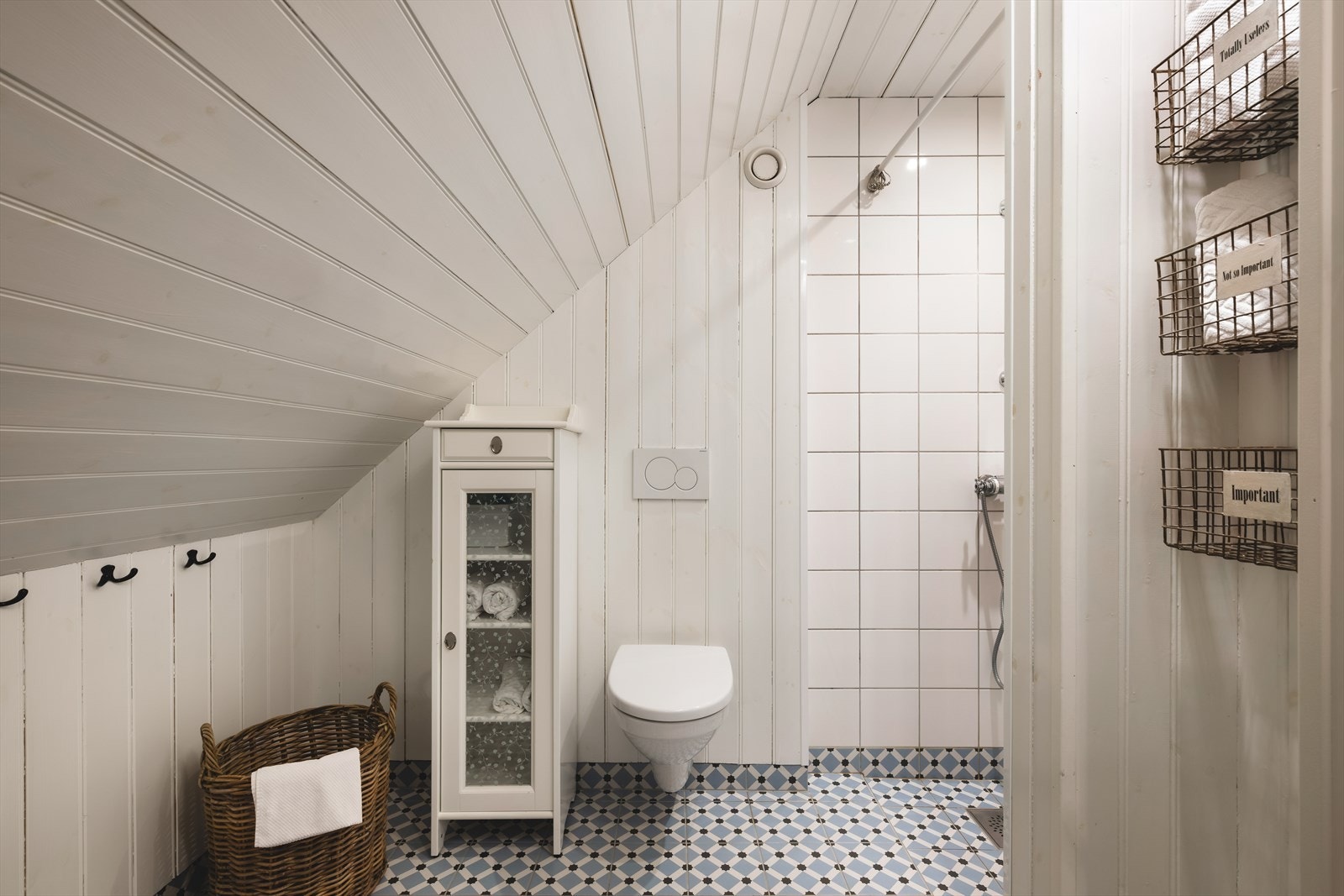 Badet er innredet med gulvstående servant, vegghengt toalett og romslig dusjhjørne med hvite fliser på vegg. Galleribilde