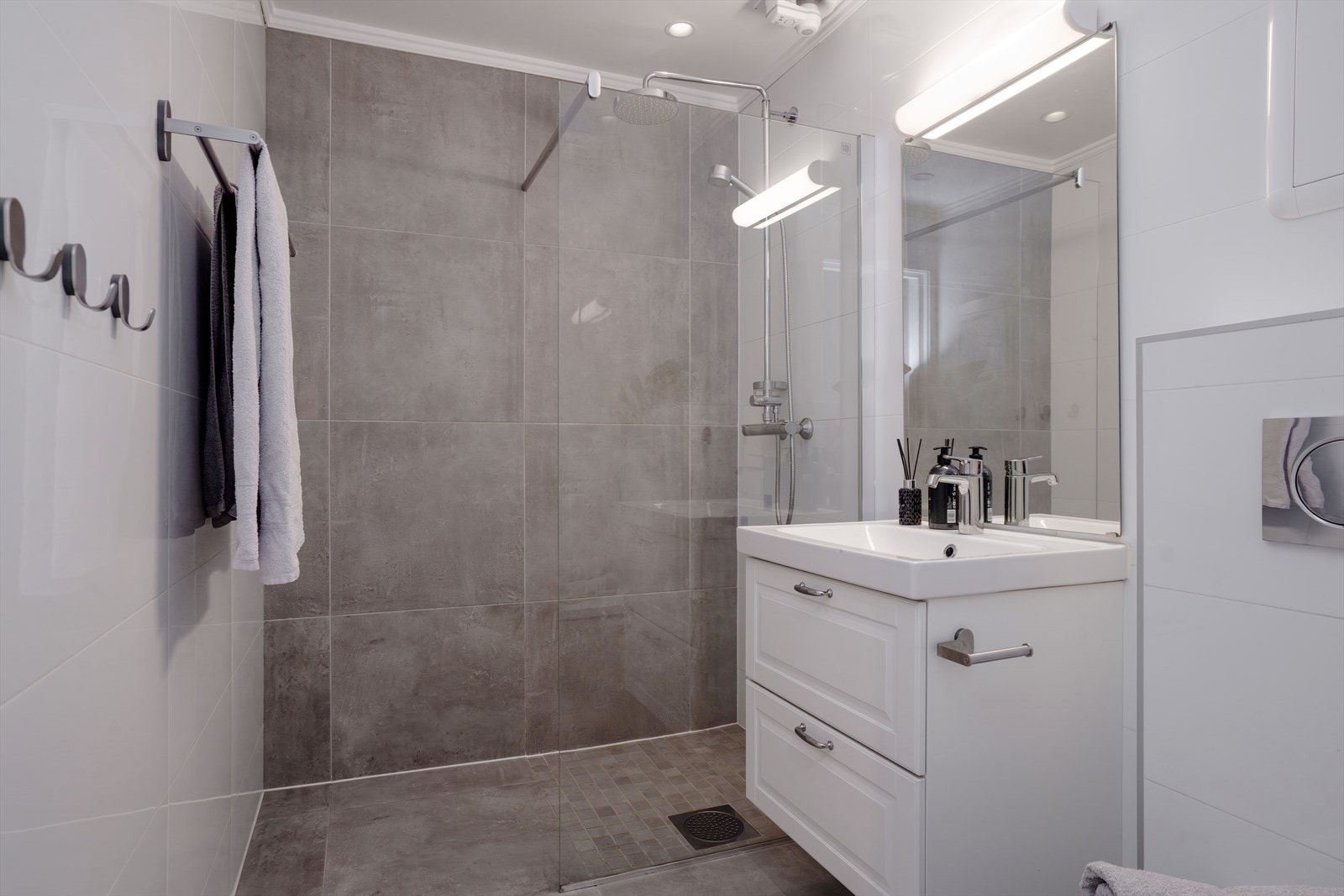 Badet har flislagte gulv og vegger og er innredet med dusjnisje, servant med innredning og veggehengt toalett. Galleribilde