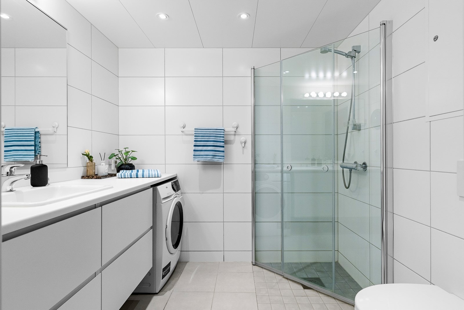 Badet er utstyrt med servant, speil, wc, dusj med innfellbare glassdører, spotter i himling, samt opplegg for vaskemaskin. Galleribilde