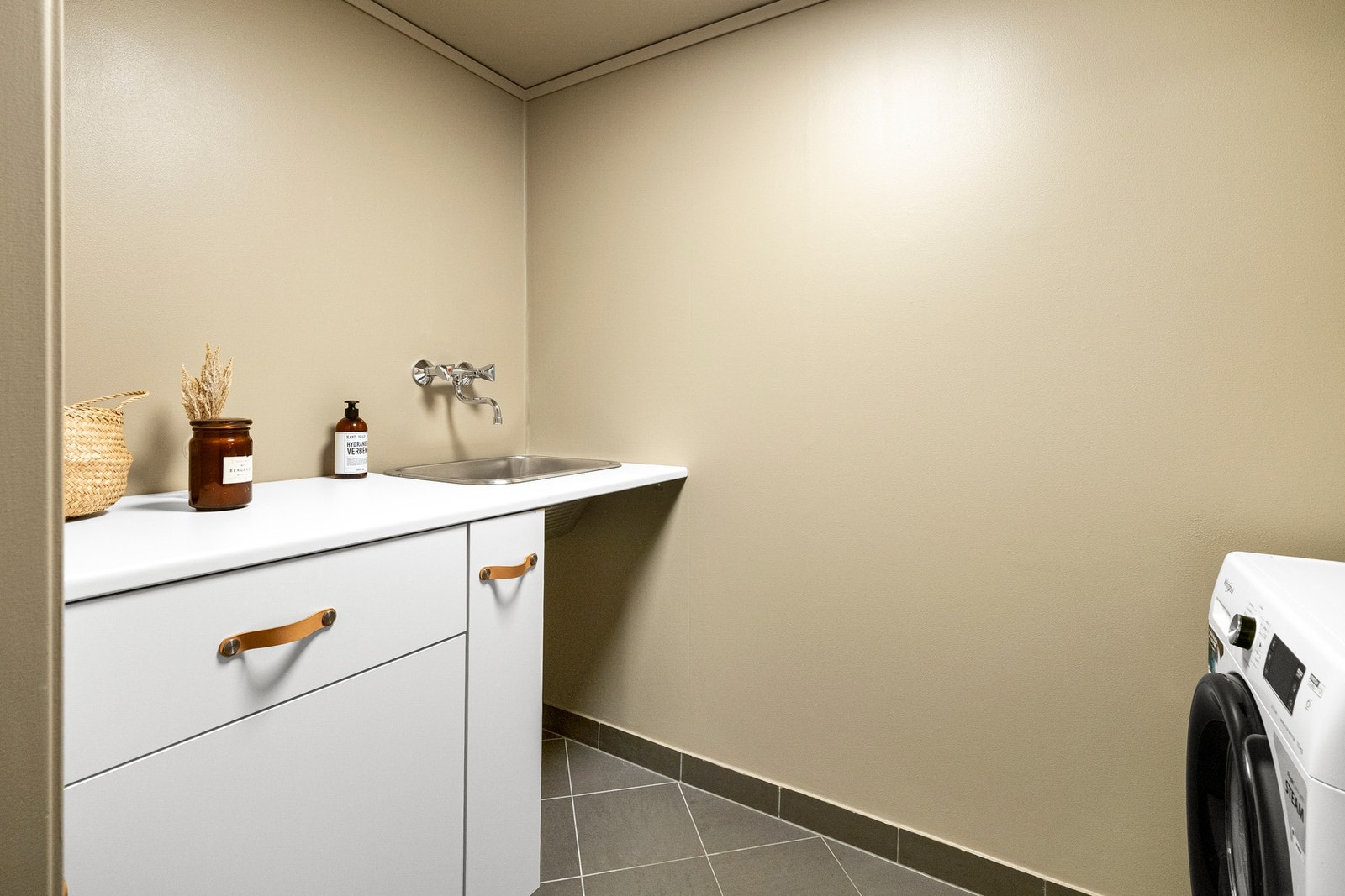 Badet er praktisk utformet med egen baderomsdel og separat vaskerom som kan lukkes med skyvedør - vaskerommet er innredet med skap, benkeplate, utslagsvask og opplegg for både vaskemaskin og tørketrommel. Galleribilde
