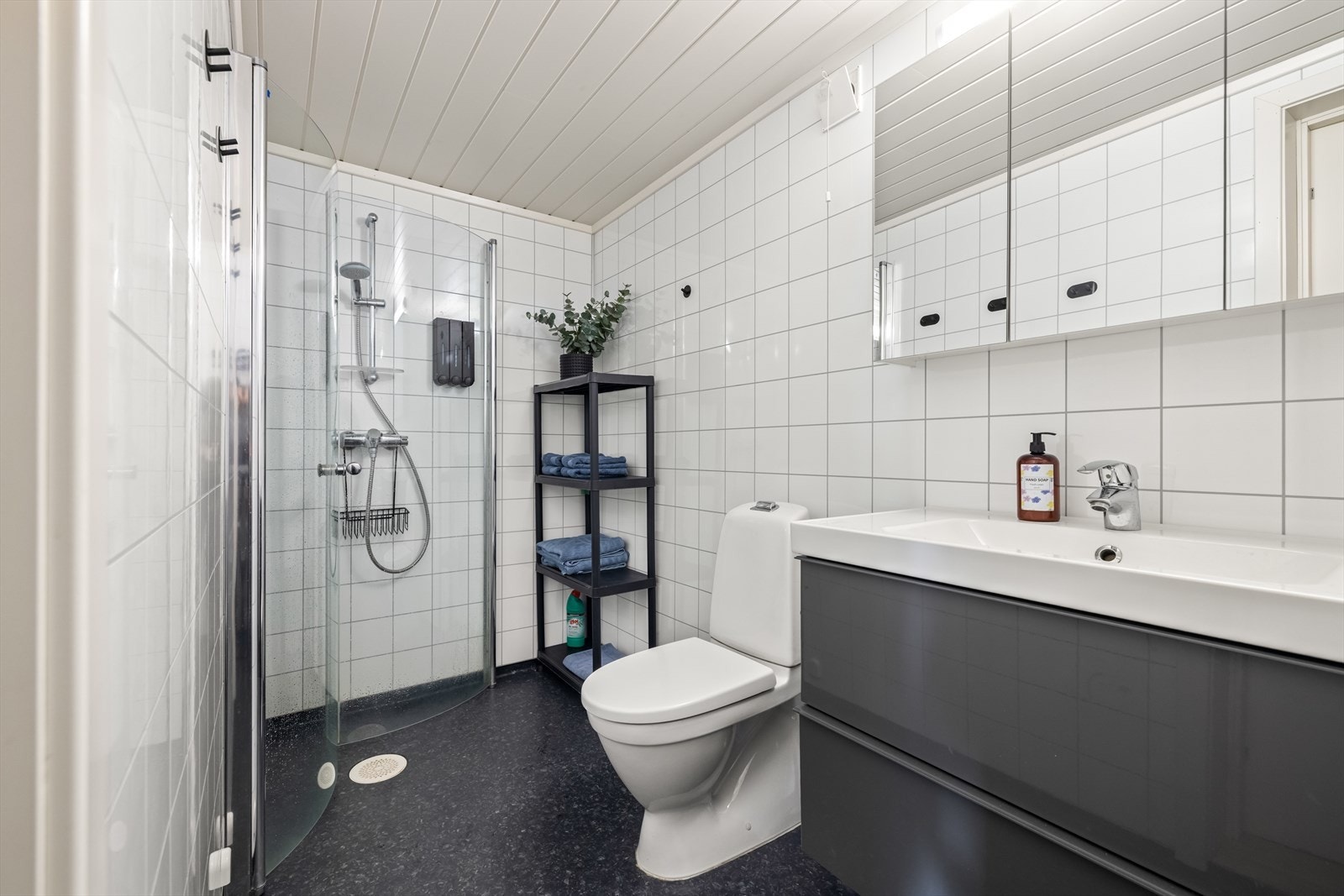 Badet tilknyttet hoveddelen har vinylbelegg på gulvet med underliggende varme, baderomsplater på veggene og panelstaver i mdf i taket. Galleribilde
