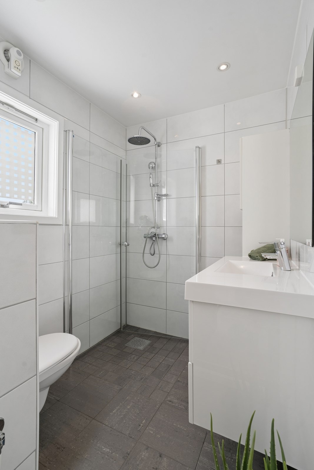 Badet er utstyrt med vegghengt toalett, dusjhjørne med svingbare glassdører, samt baderomsinnredning med servant og speil. Galleribilde