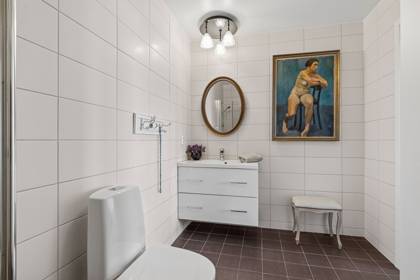 Badet er stilrent utført med flislagte gulv og vegger, samt malt betong i taket som gir et moderne preg. Innredningen består av servantskap, toalett og dusjnisje med glassdører. Rommet er mekanisk ventilert. Galleribilde