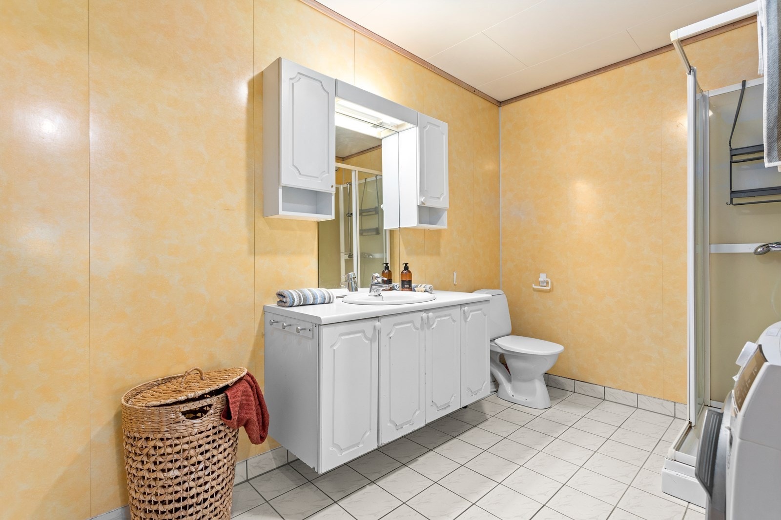 Badet er eit kombinert vaskerom med flis på golv og baderomsplater på veggar. I taket er det kvite plater. Galleribilde