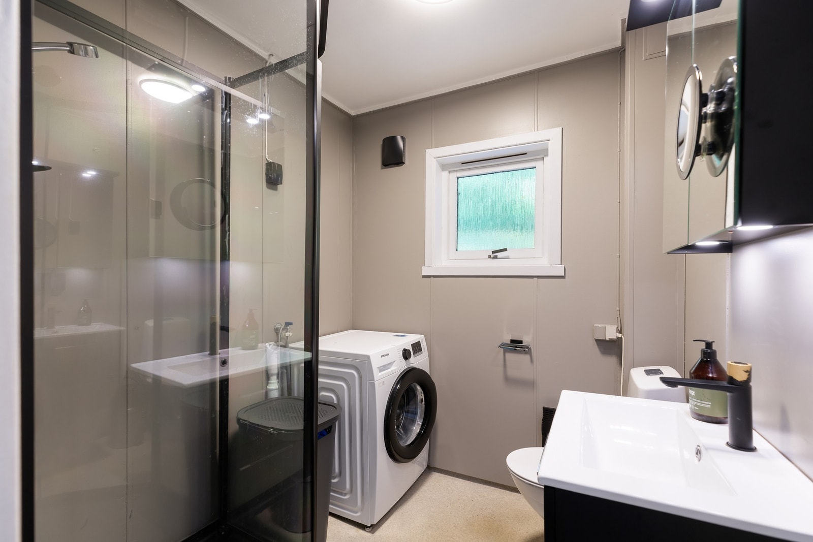 Bad i kjeller med elektrisk gulvvarme. Badet er innredet med toalett, servant, speilskap med lys og dusjkabinett. Galleribilde