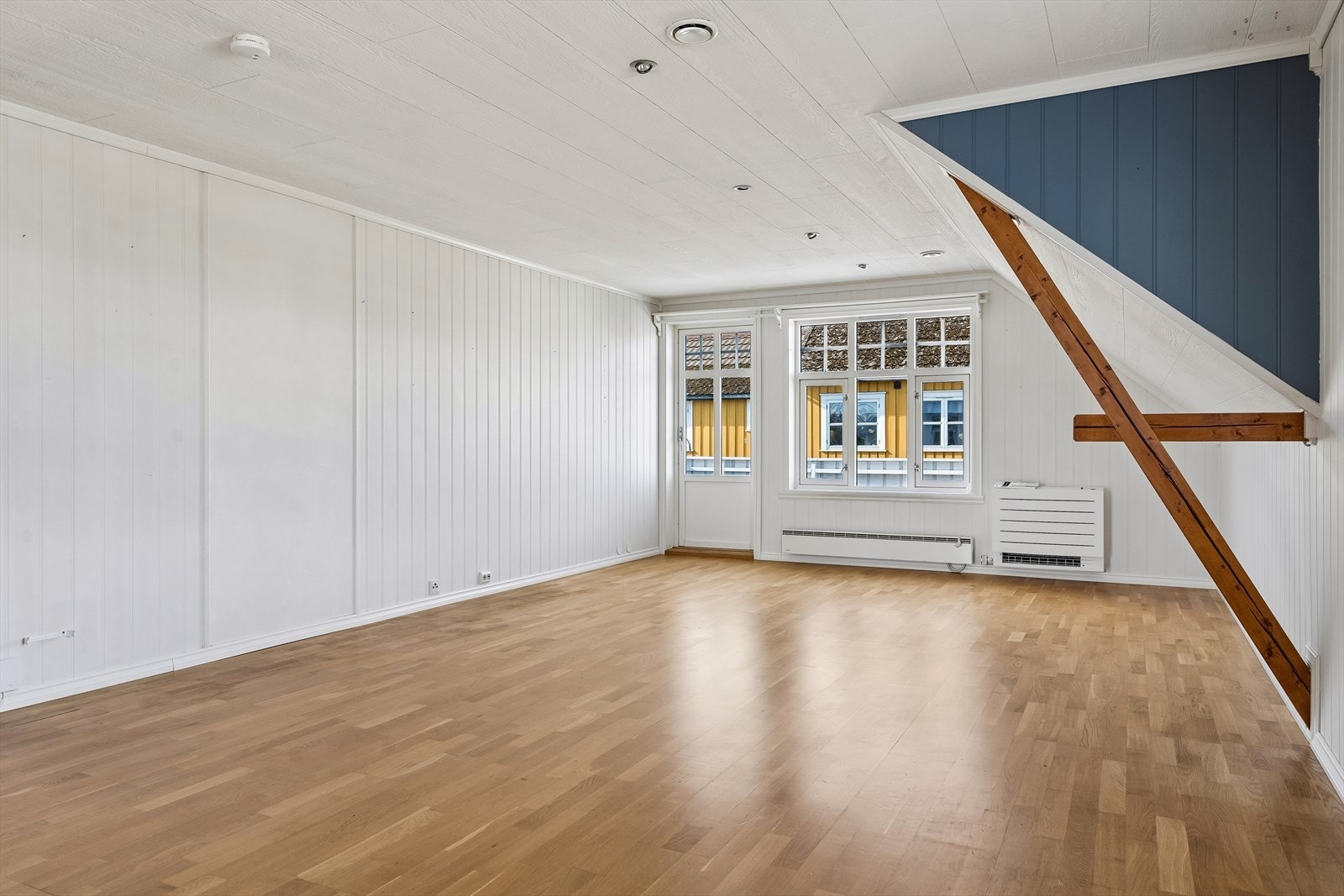 Romslig stue med parkettgulv og lyse vegger, samt adkomst til utendørs balkong Galleribilde