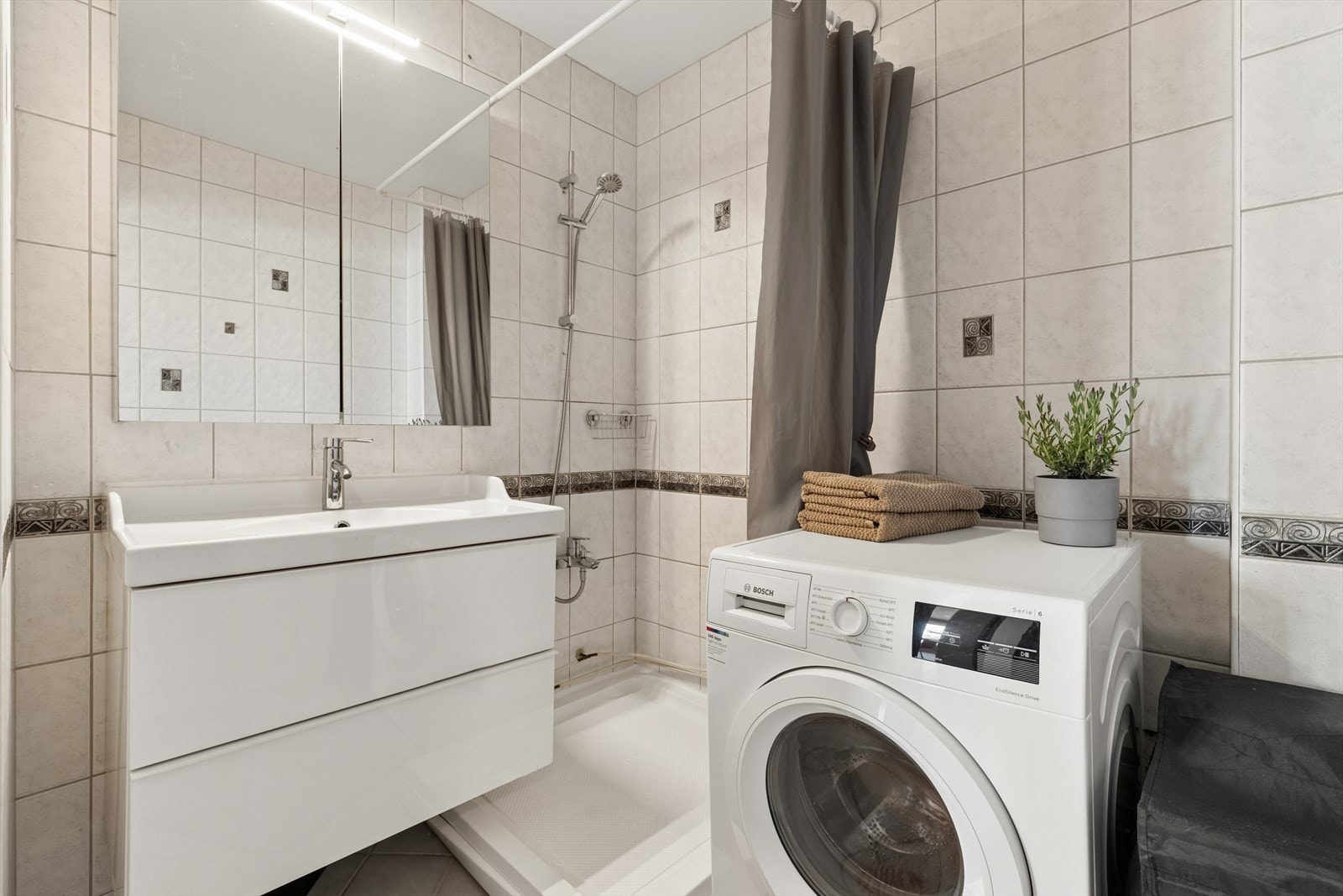 Badet er flislagt og utstyrt med dusjhjørne, servantinnredning og opplegg for vaskemaskin. Galleribilde