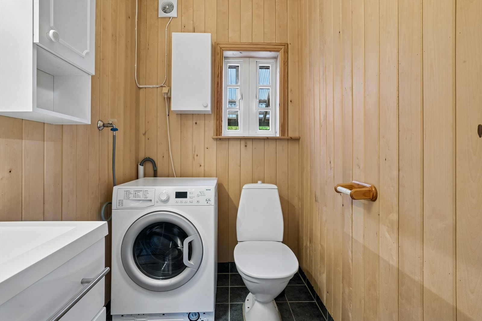 Badet har gulvstående toalett, heldekkende servant i innredning, dusjkabinett, samt opplegg for vaskemaskin. Galleribilde