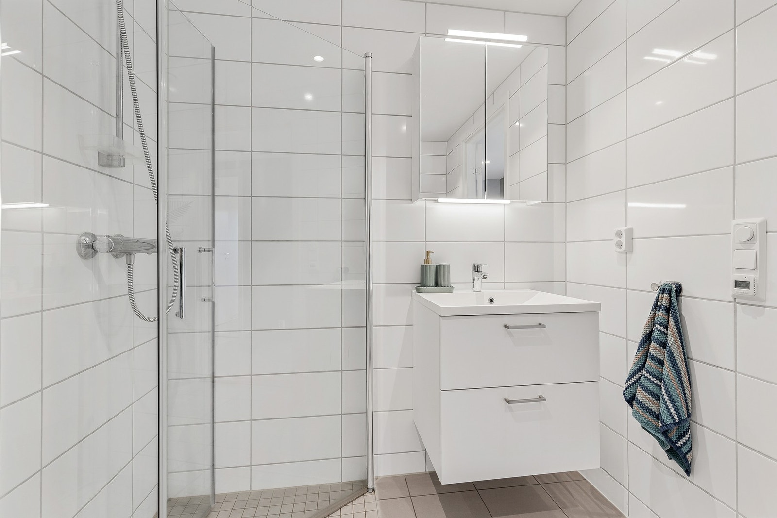 Badet har innredning med nedfelt servant, veggmontert toalett og dusjhjørne med innfellbare vegger Galleribilde