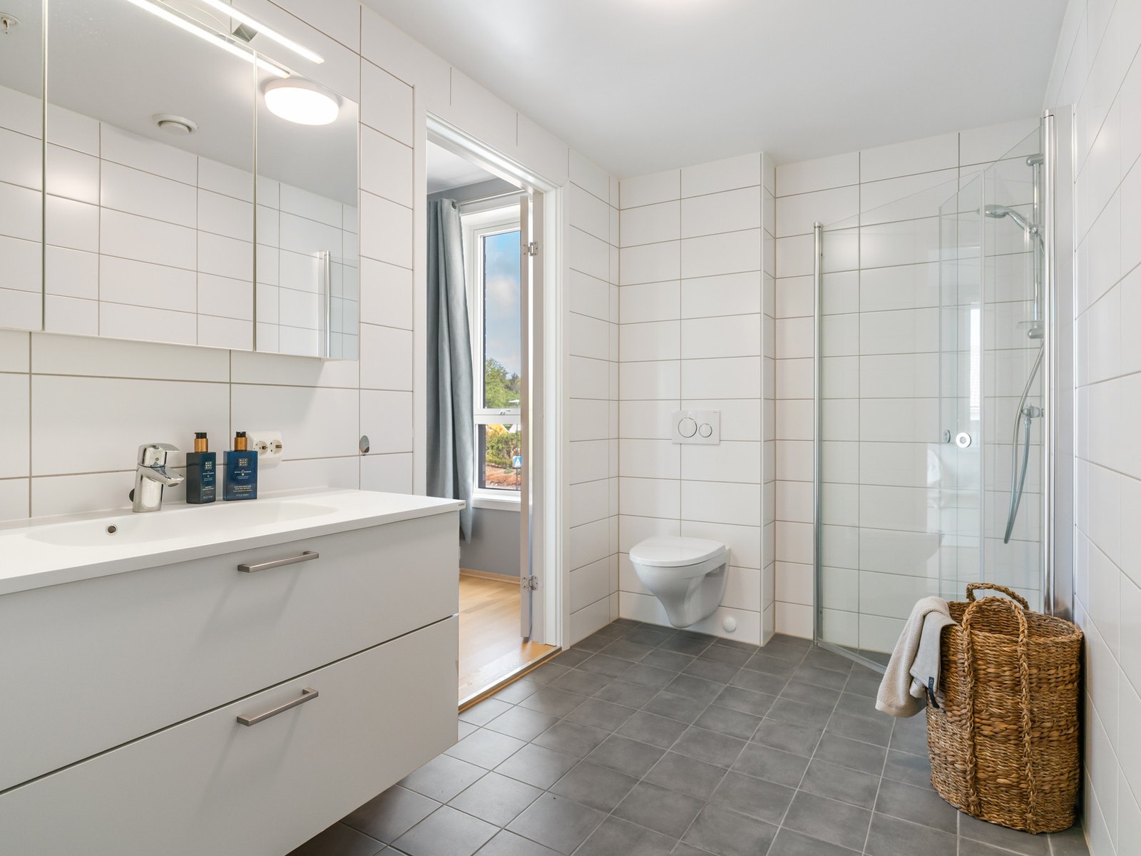 Badet har fliser på både gulv og vegger, samt gulvvarme. Badet er innredet med servant på skuffeseksjon og speil. Videre er rommet utstyrt med toalett og dusj. Galleribilde