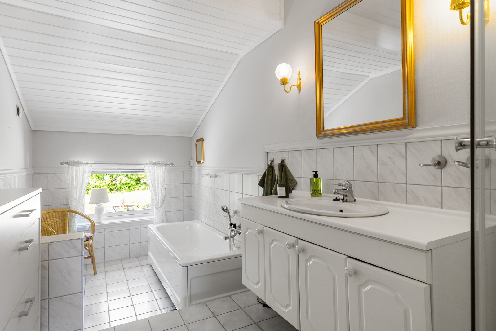 Romslig baderom innredet med badekar, dusjkabinett, servant med skap og toalett. Galleribilde