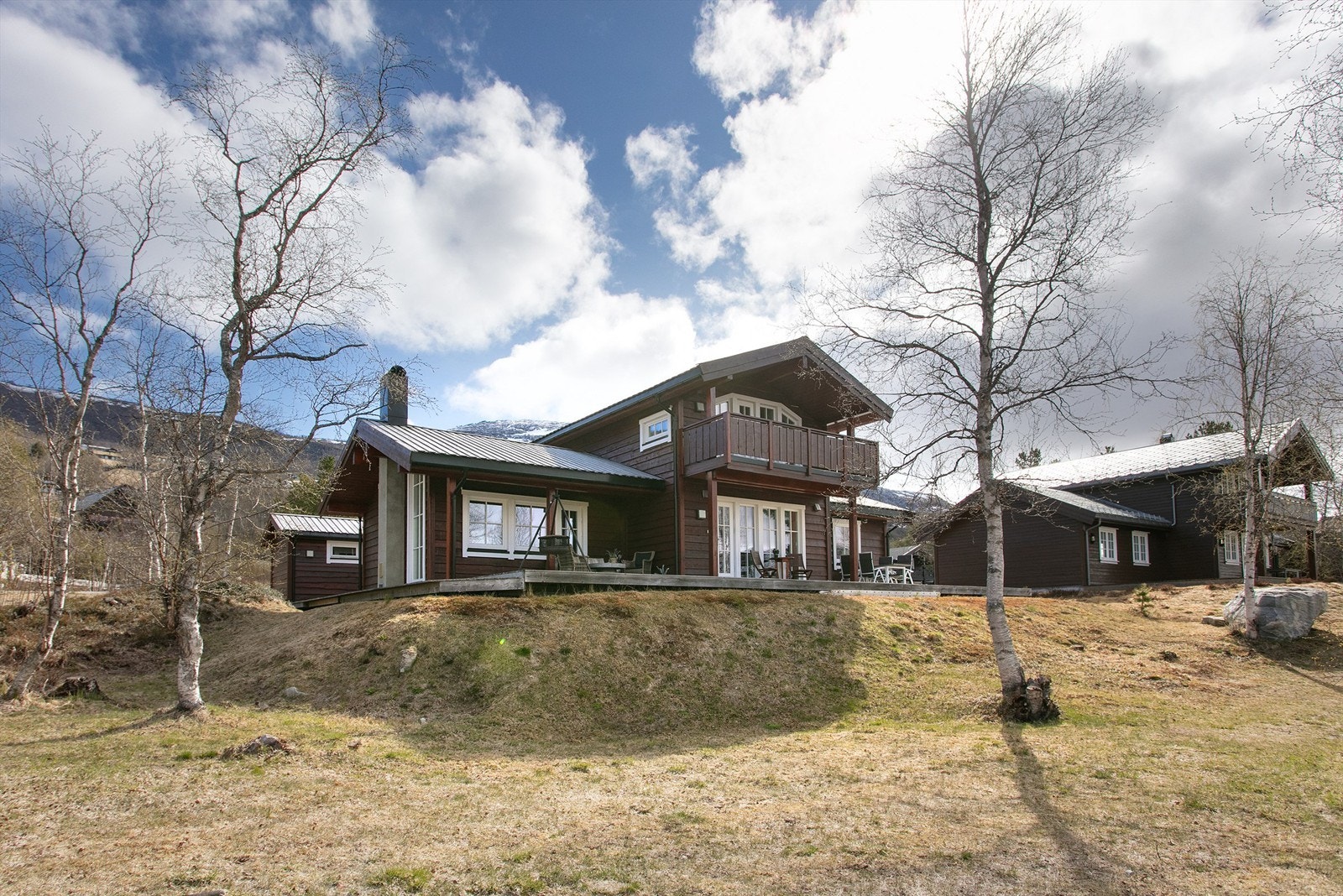 Hytta ligger fint til i terrenget, omgitt av bjørkeskog og med utsikt mot fjellene. Galleribilde
