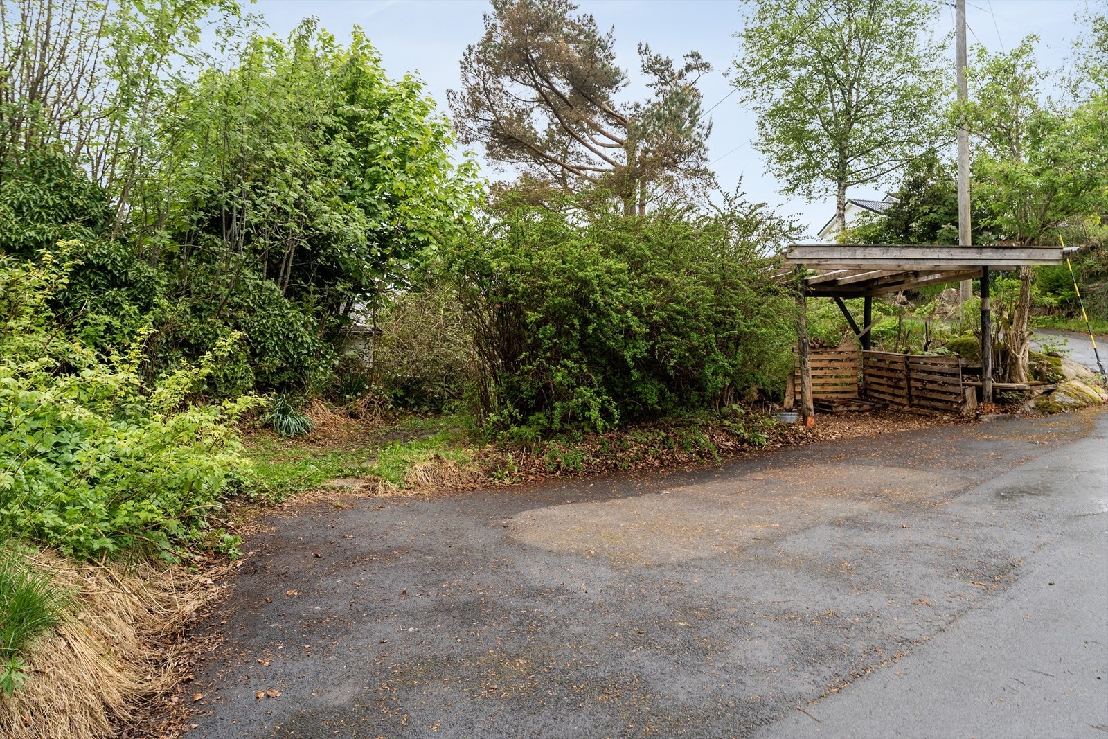 Parkering skjer i asfaltert gårdsrom med tilhørende eldre carport. Fra parkeringsplassen er det gangvei videre inn til hytten og uteområdet. Galleribilde
