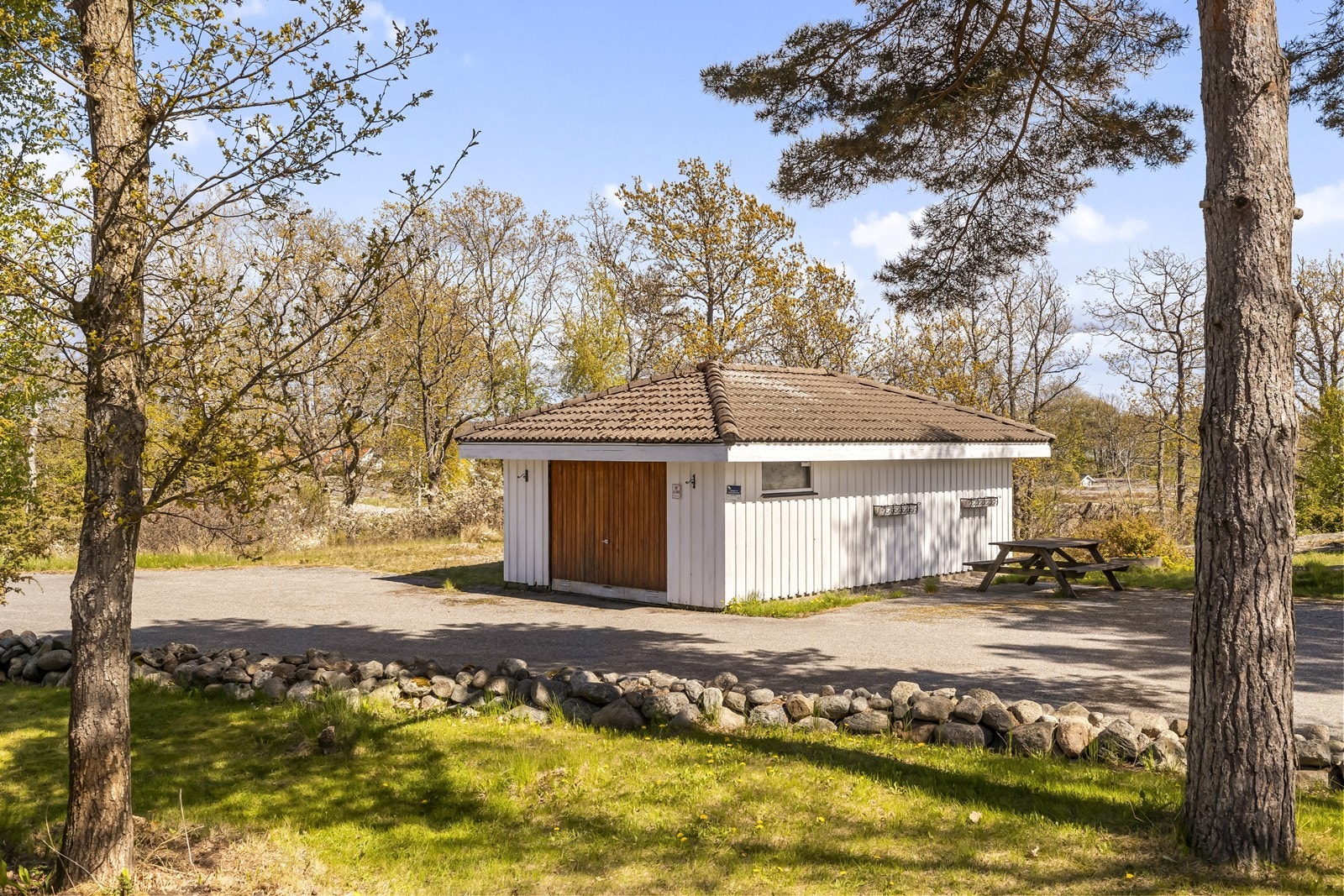 Frittstående garasje med leddport i tre. Garasjen ble malt i 2023. Flere biloppstillingsplasser er det på begge sider av denne. Galleribilde