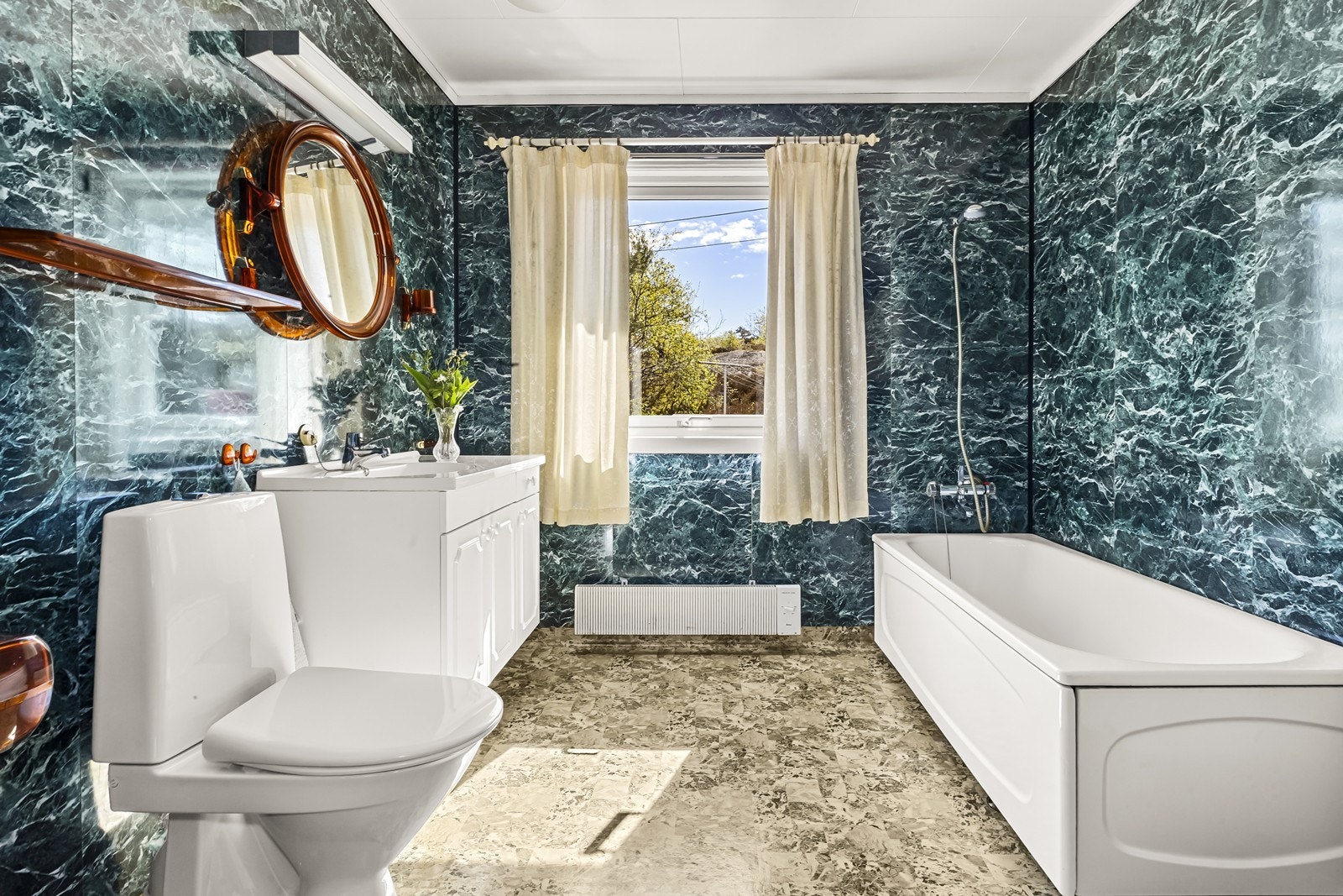 Badet ligger vegg i vegg med soverommet. Våtromsplater på vegger og beleggg på gulvet. Servantinnredning med hvite profilerte fronter og heldekkende servant. Galleribilde