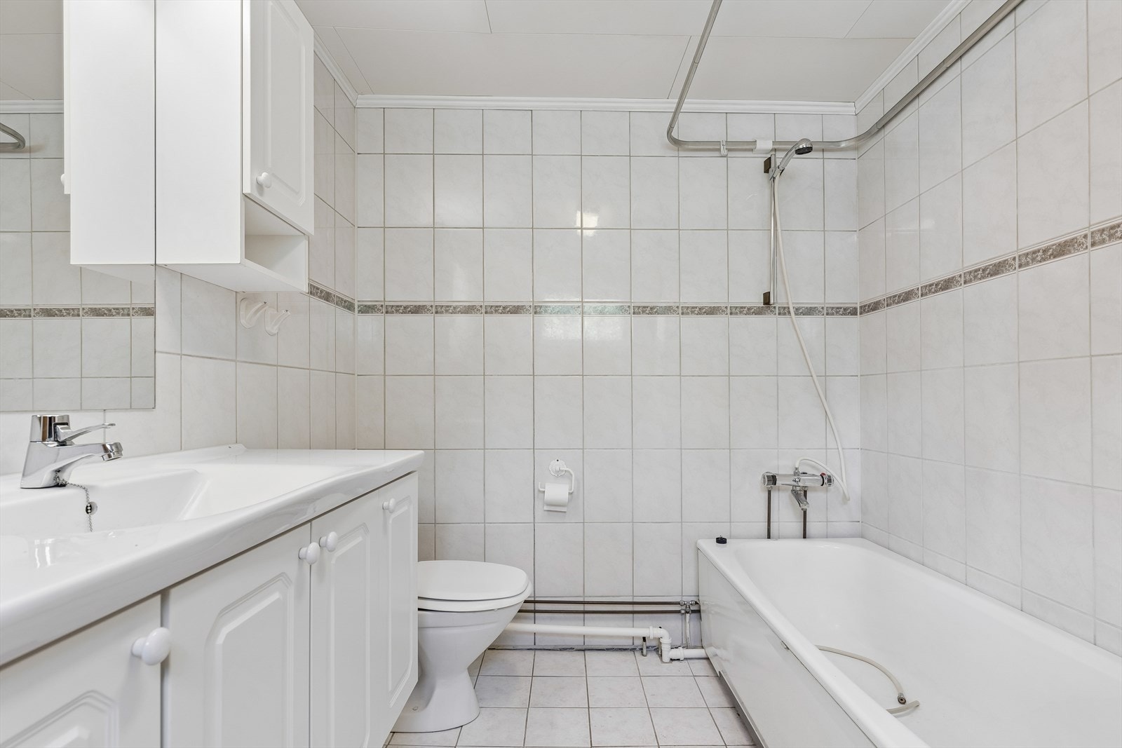 Flislagt bad i første etasje, utstyrt med badekar, toalett og baderomsinnredning med servant. Galleribilde