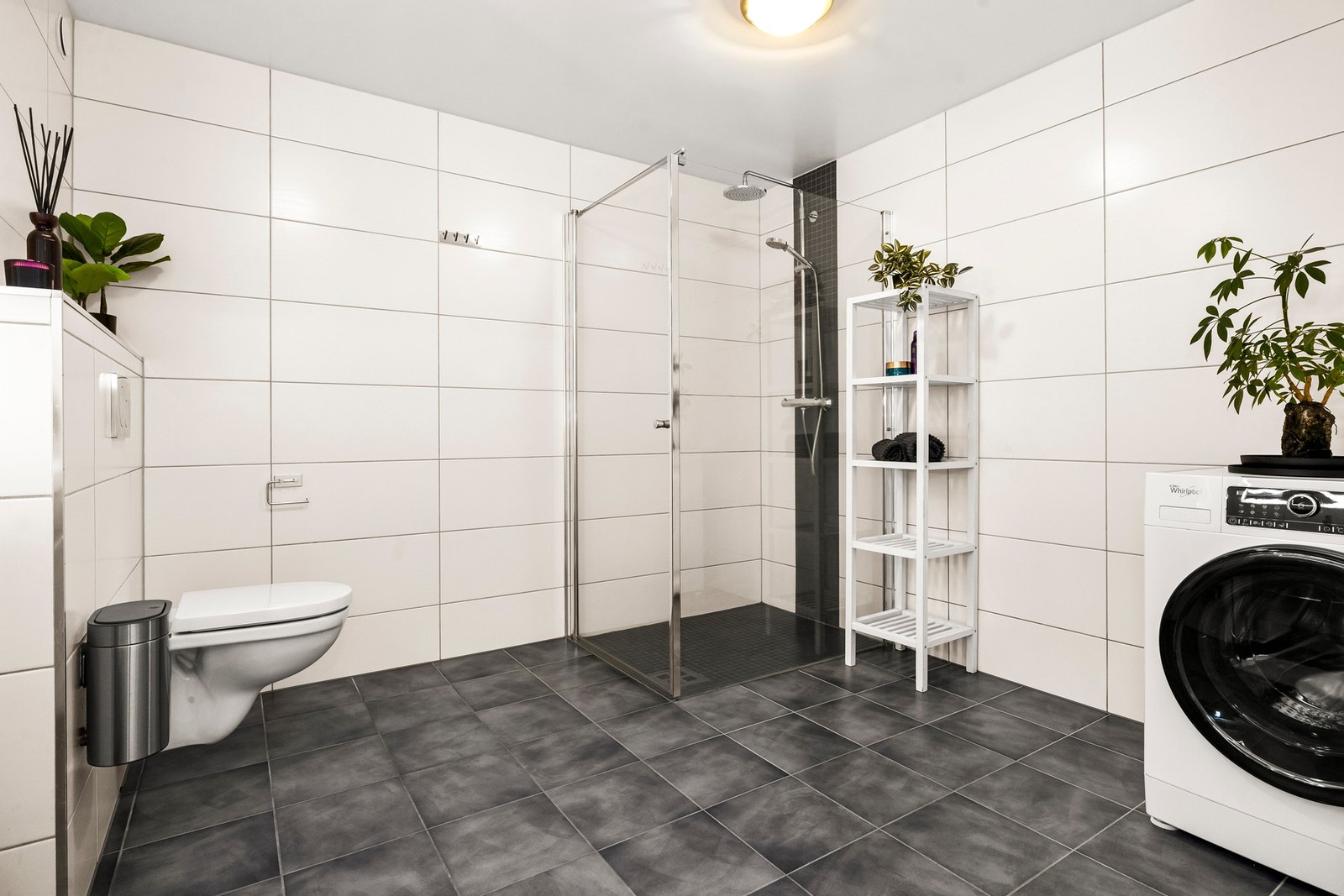 Badet er utstyrt med varmekabler i gulv, vegghengt toalett, dusjhjørne, servantinnredning og opplegg for vaskemaskin Galleribilde