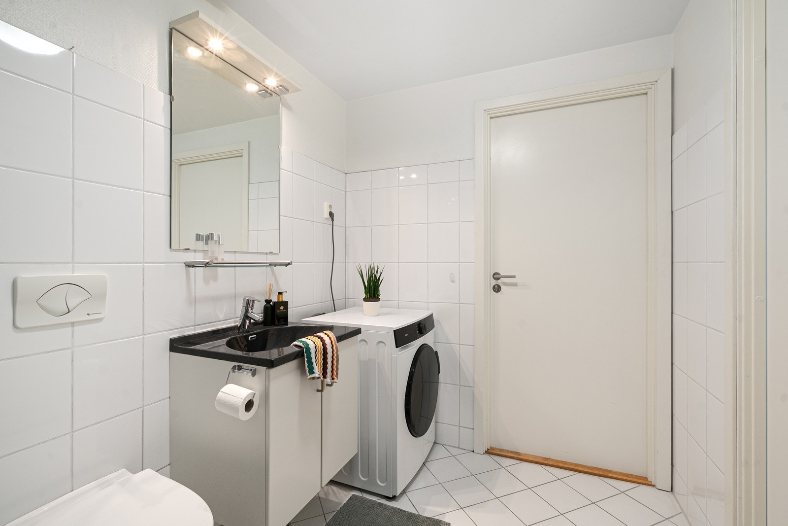 Badet er helfliset og har elektriske varmekabler som gir god komfort året rundt. Rommet har innredning med nedfelt servant i skapseksjon, veggmontert toalett og dusjkabinett. Det er også opplegg for vaskemaskin. Galleribilde