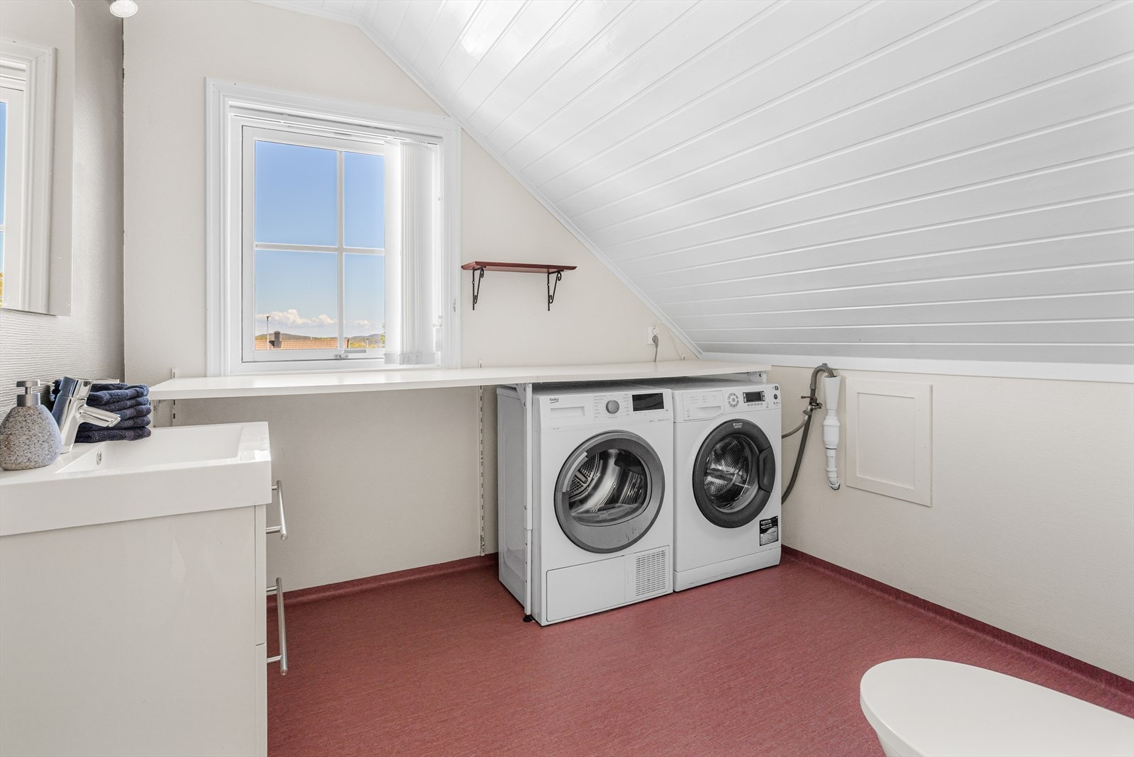 Praktisk vaskerom på loftet med vinylbelegg på gulv, arbeidsbenk og opplegg for vaskemaskin. Galleribilde