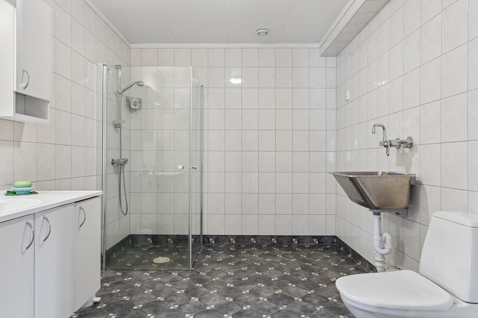 Badet er utstyrt med dusjdører i glass, toalett, servantinnredning og et praktisk skyllekar. Galleribilde