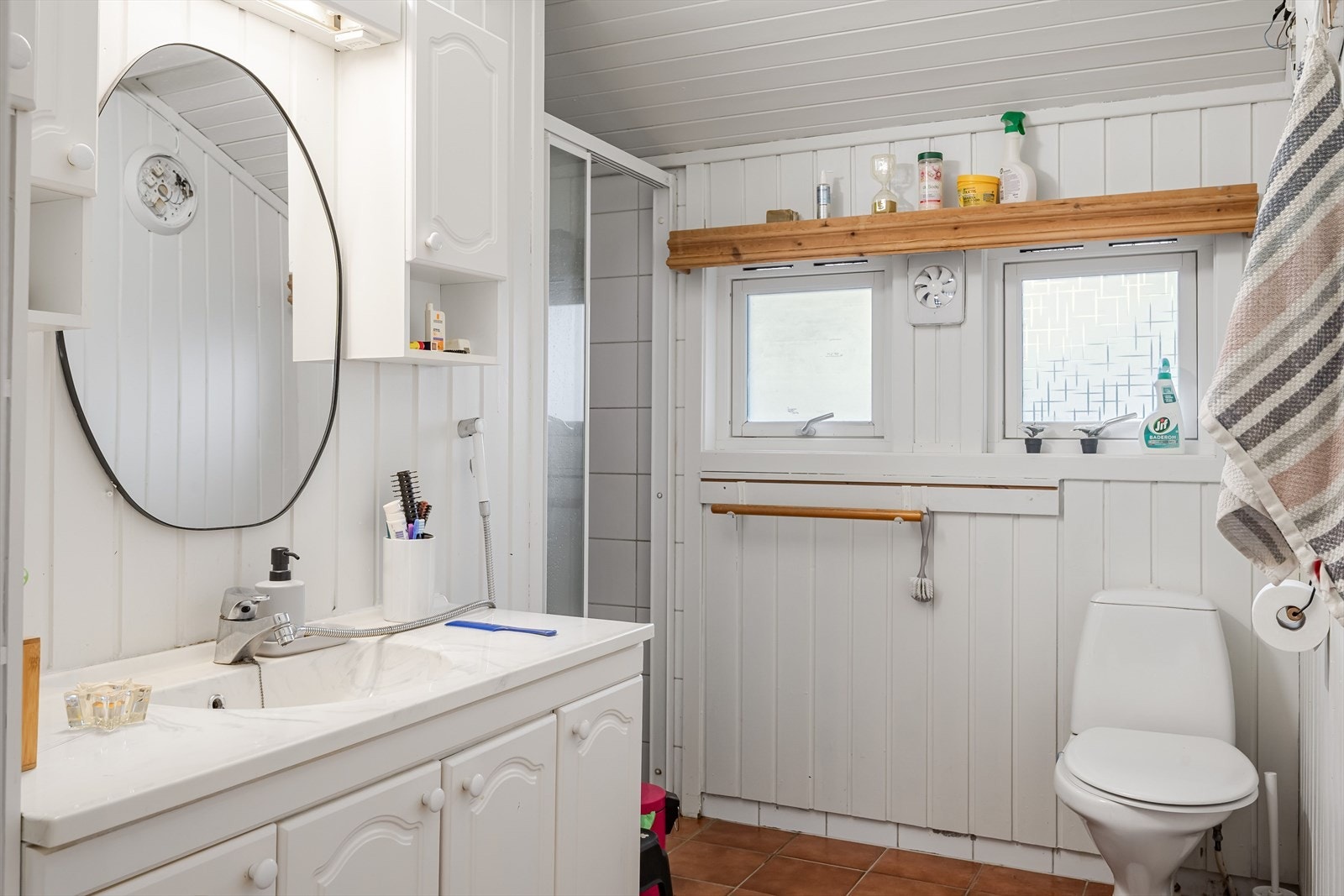 Baderom i 1. etasje med med ukjent alder. Baderommet har flislagt gulv, elektrisk gulvvarme, overflater med fliser og malt panel, samt elektrisk styrt vifte. Galleribilde
