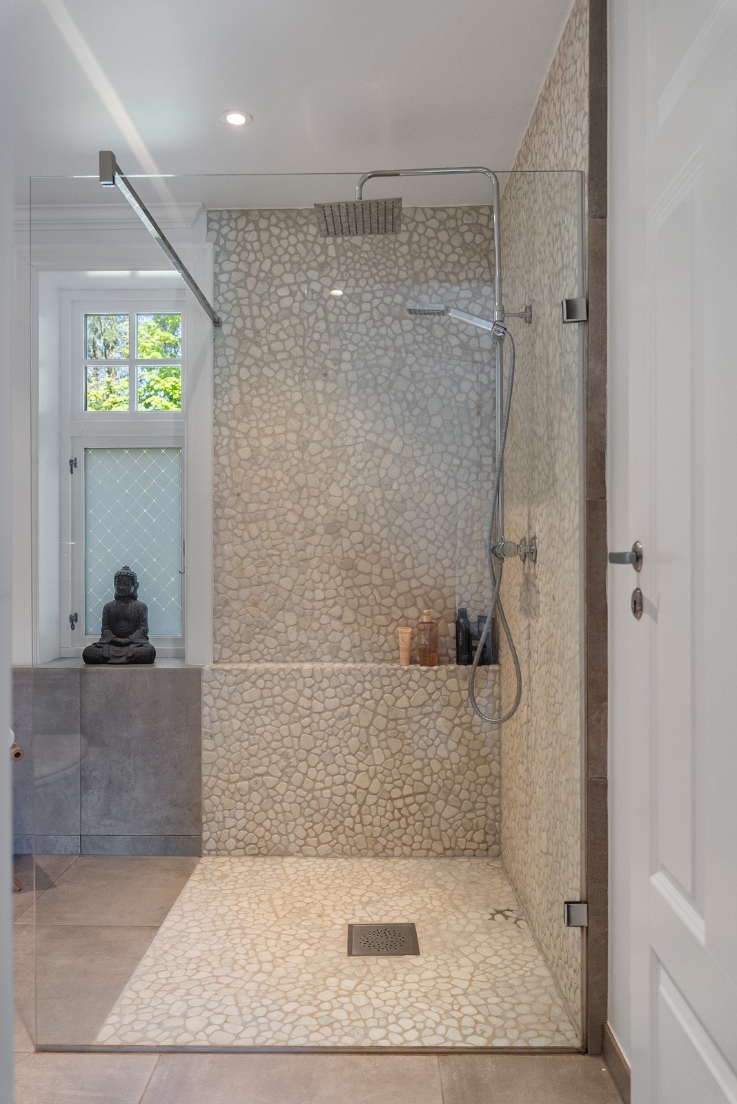 Badet inneholder servant i møblement, speil, og vegghengt toalett, i tillegg til en romslig dusjsone med skillevegg i glass. Galleribilde
