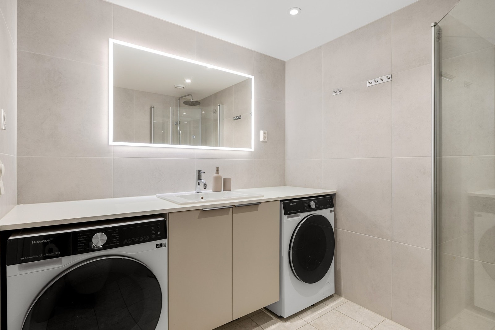 Badet inneholder innfellbare og plassbesparende dusjdører i glass, vannbåren varme i gulv, innfelte downlights i himling, kran og avløp for vaskemaskin og veggmontert WC. Galleribilde