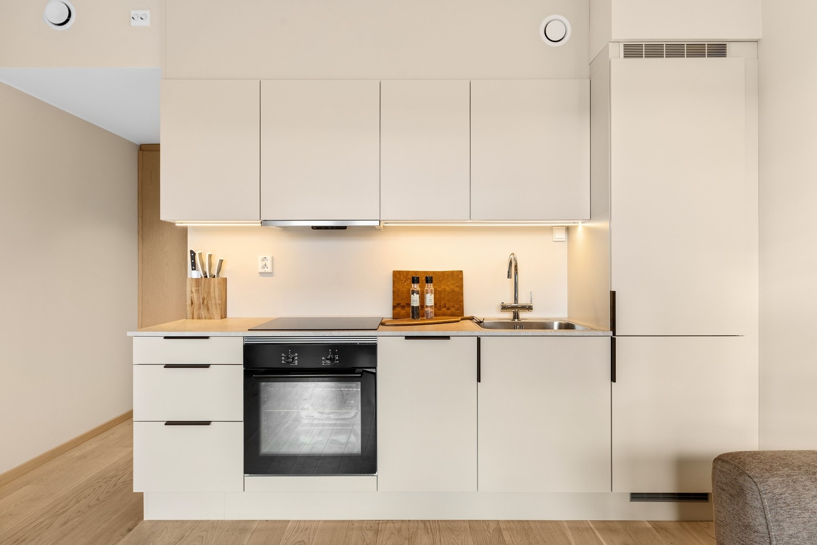 Leilighetens moderne kjøkken med sin lune og pene fargetone inneholder integrerte hvitevarer som platetop, stekeovn, oppvaskmaskin og kjøl/fryseskap. Galleribilde