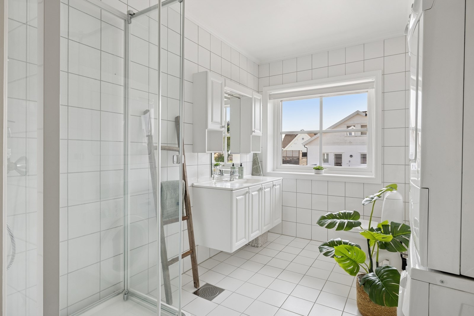Badet er fliser på gulv og vegger. Dusjkabinett, servant med skap og sideskap ved speilet. Galleribilde