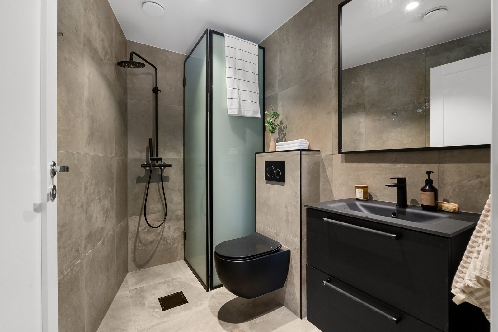 Badet tilknyttet hovedsoverommet har flislagte vegger, flislagt gulv, varmekabler og nedsenket malt himling med downlights. Rommet er innredet med servantinnredning med skuffer, speil med takbelysning, åpen dusj og veggmontert toalett. Galleribilde
