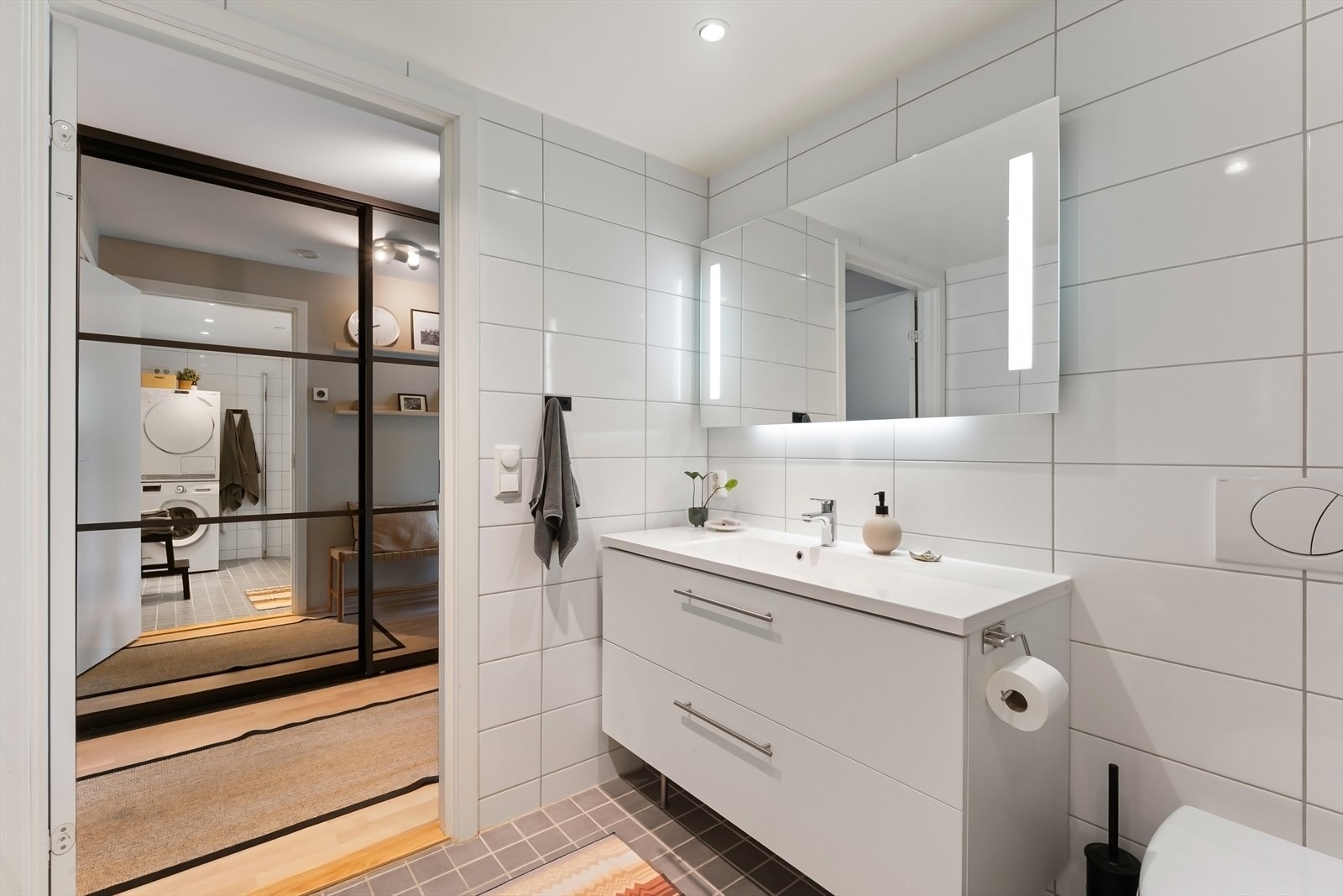 Badet er utstyrt med servant med skuffer, ledspeil, dushjørne og veggmontert toalett. Galleribilde
